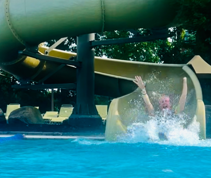 ID: Woman sliding down a water slide with her hands in the air. One hand is limb different.
