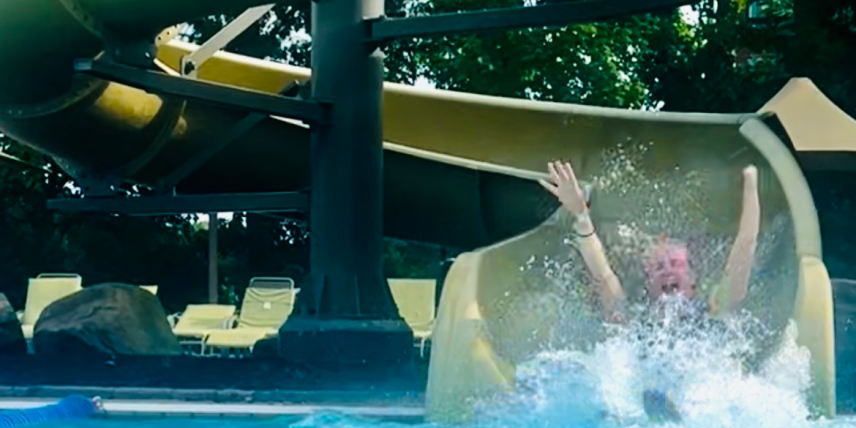 ID: Woman sliding down a water slide with her hands in the air. One hand is limb different.