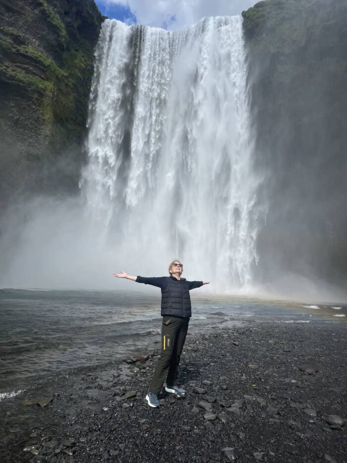 woman with arms outstretched at the skógafoss waterfall in Iceland.