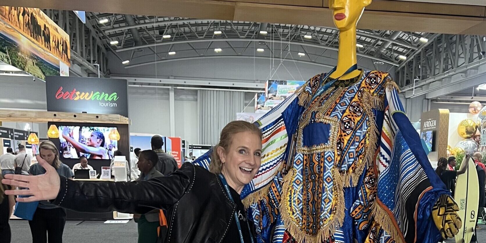 ID: Me (white female) posing with arms outstretched next to a tall, colorful, stylized figure in traditional African attire. At WTM Africa