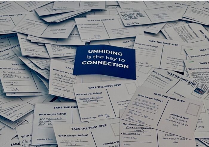Pile of handwritten postcards answering the question “What are you hiding?” with a blue card in the center reading “Unhiding is the key to Connection."