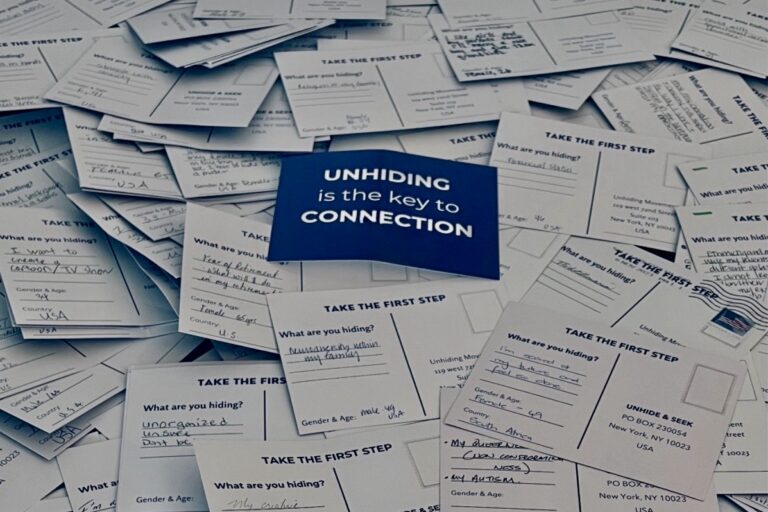Pile of handwritten postcards answering the question “What are you hiding?” with a blue card in the center reading “Unhiding is the key to Connection."