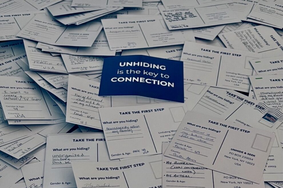 Pile of handwritten postcards answering the question “What are you hiding?” with a blue card in the center reading “Unhiding is the key to Connection."